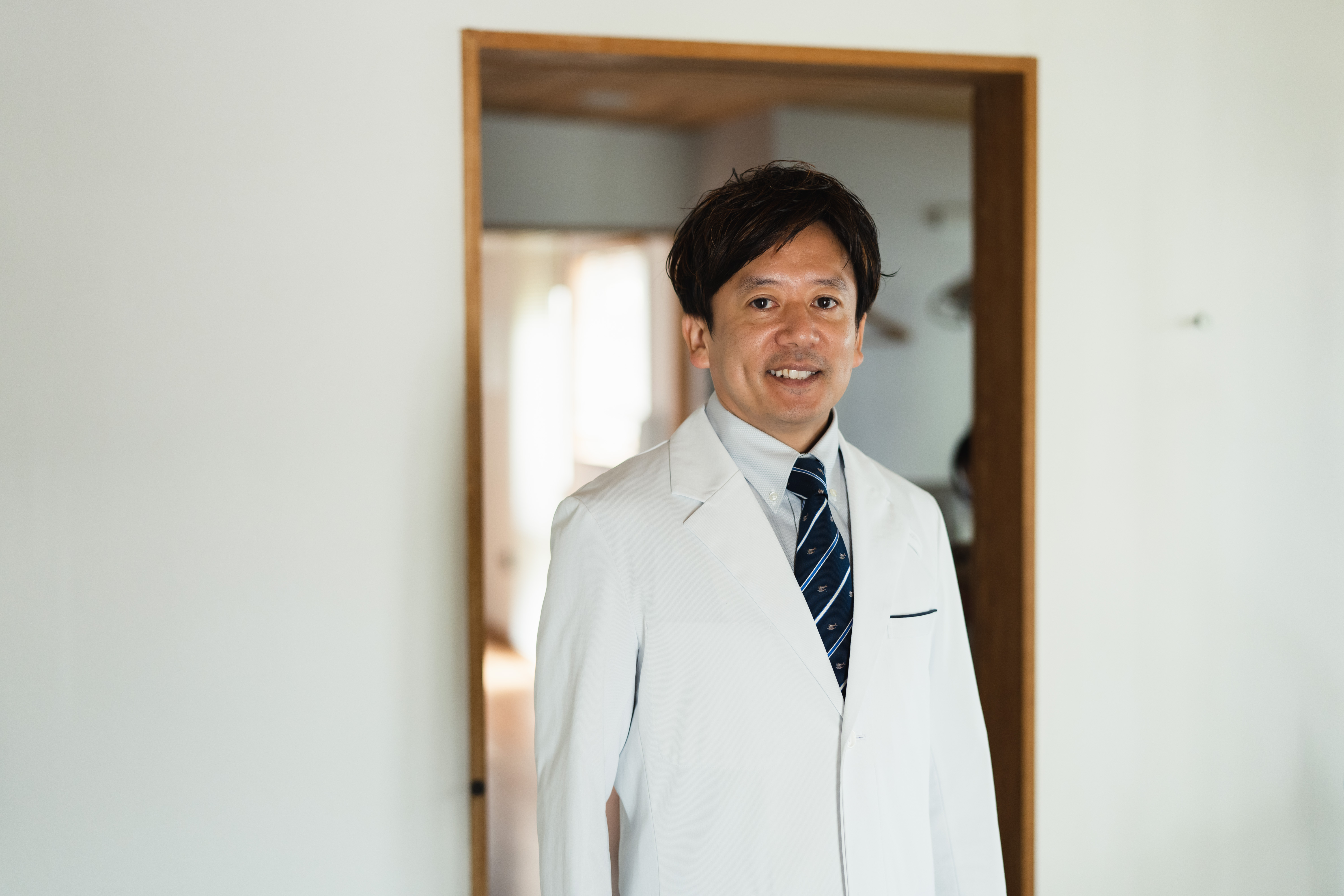 白衣を着た男性歯科医師が室内で前向きに立つ